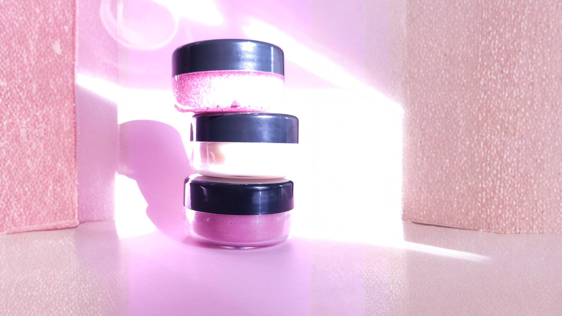 Stack of cylindrical containers with black lids on a pink textured background