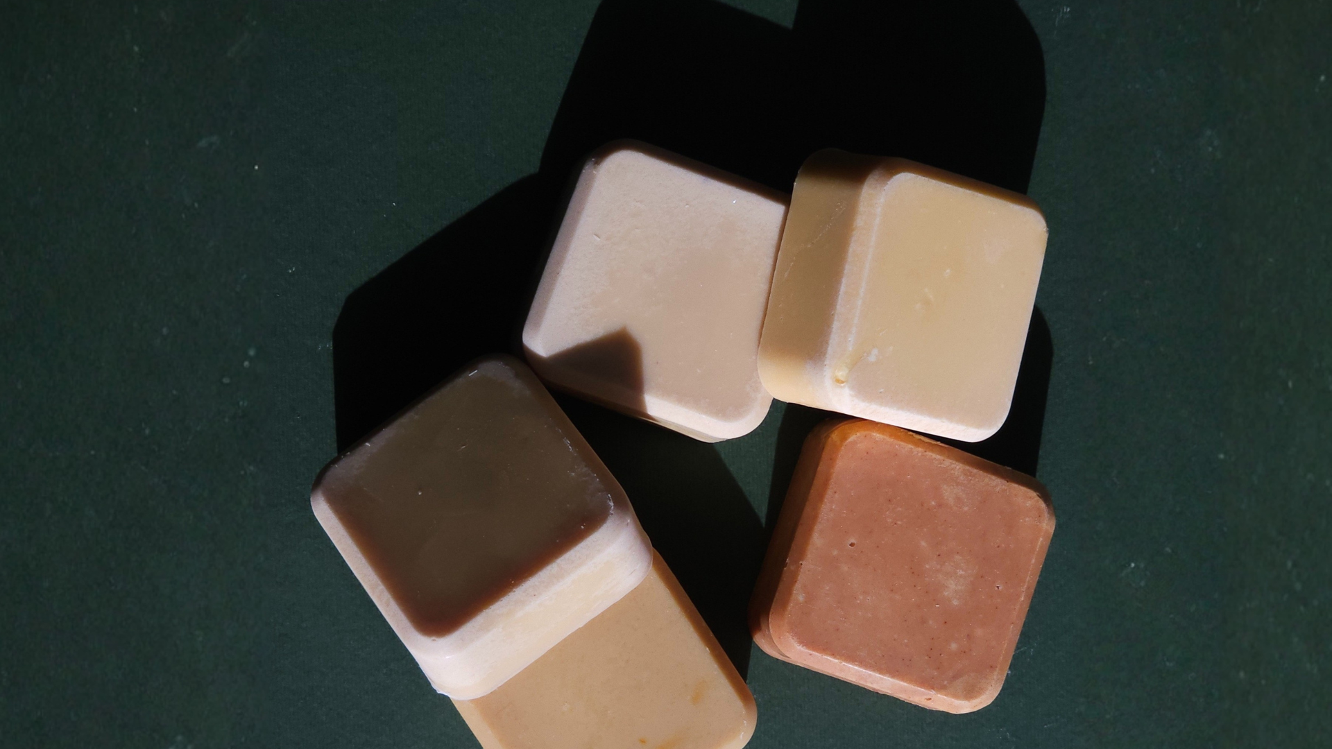 Five square-shaped cookies in different shades of brown on a dark surface